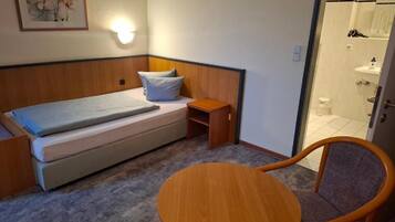 Ein kleines Zimmer mit einem Bett, einem Nachttisch, einem Stuhl und einer Dusche.