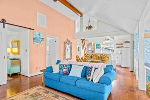 A living room with a blue sofa, a dining area with a wooden table and chairs, and a kitchen in the background.
