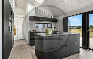 A modern kitchen with a central island, built-in appliances, and a large window offering a view of the outdoors. - Awesome home in Jerup with sauna (Jerup)