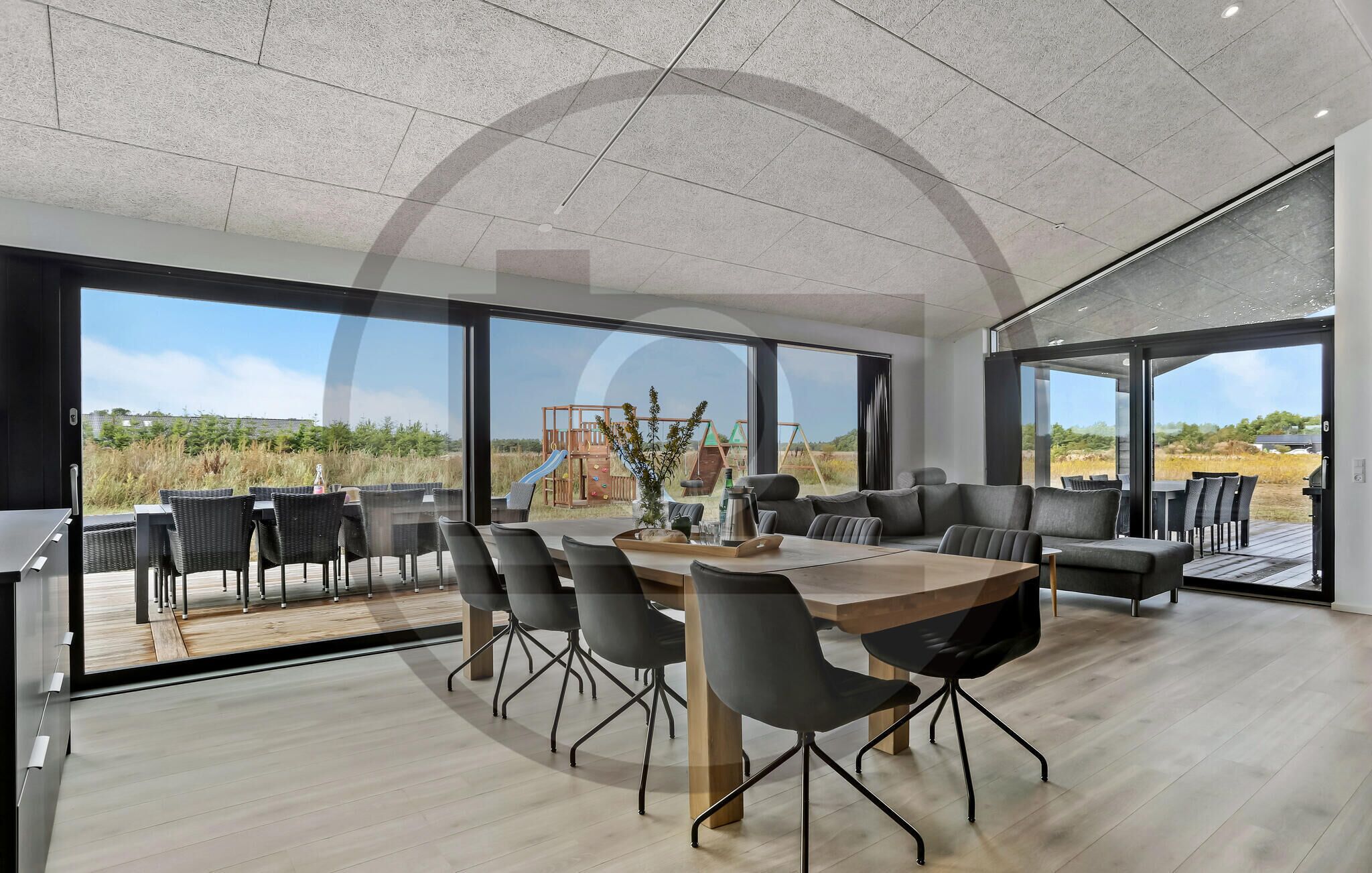 A modern dining area with a wooden table and black chairs, large windows, and a view of a playground.