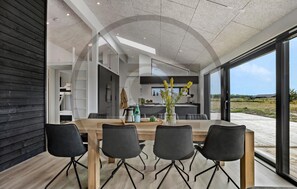 A modern dining area with a wooden table and black chairs, a kitchen in the background, and a view of the outdoors. - Awesome home in Jerup with sauna (Jerup)