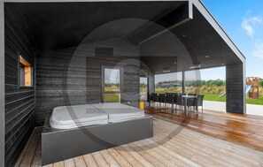 A modern outdoor hot tub area with a wooden deck, a dining table with chairs, and a view of the landscape. - Awesome home in Jerup with sauna (Jerup)