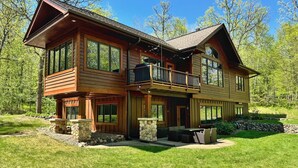 Une cabane en rondins à deux étages, dotée d’un balcon, d’éléments décoratifs en pierre et d’une pelouse bien entretenue.