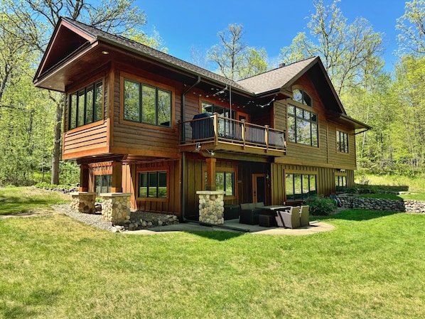 A two-story log cabin with a balcony, stone accents, and a well-maintained lawn.