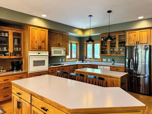 A kitchen with wooden cabinets, a stainless steel refrigerator, a white countertop, and a large island.