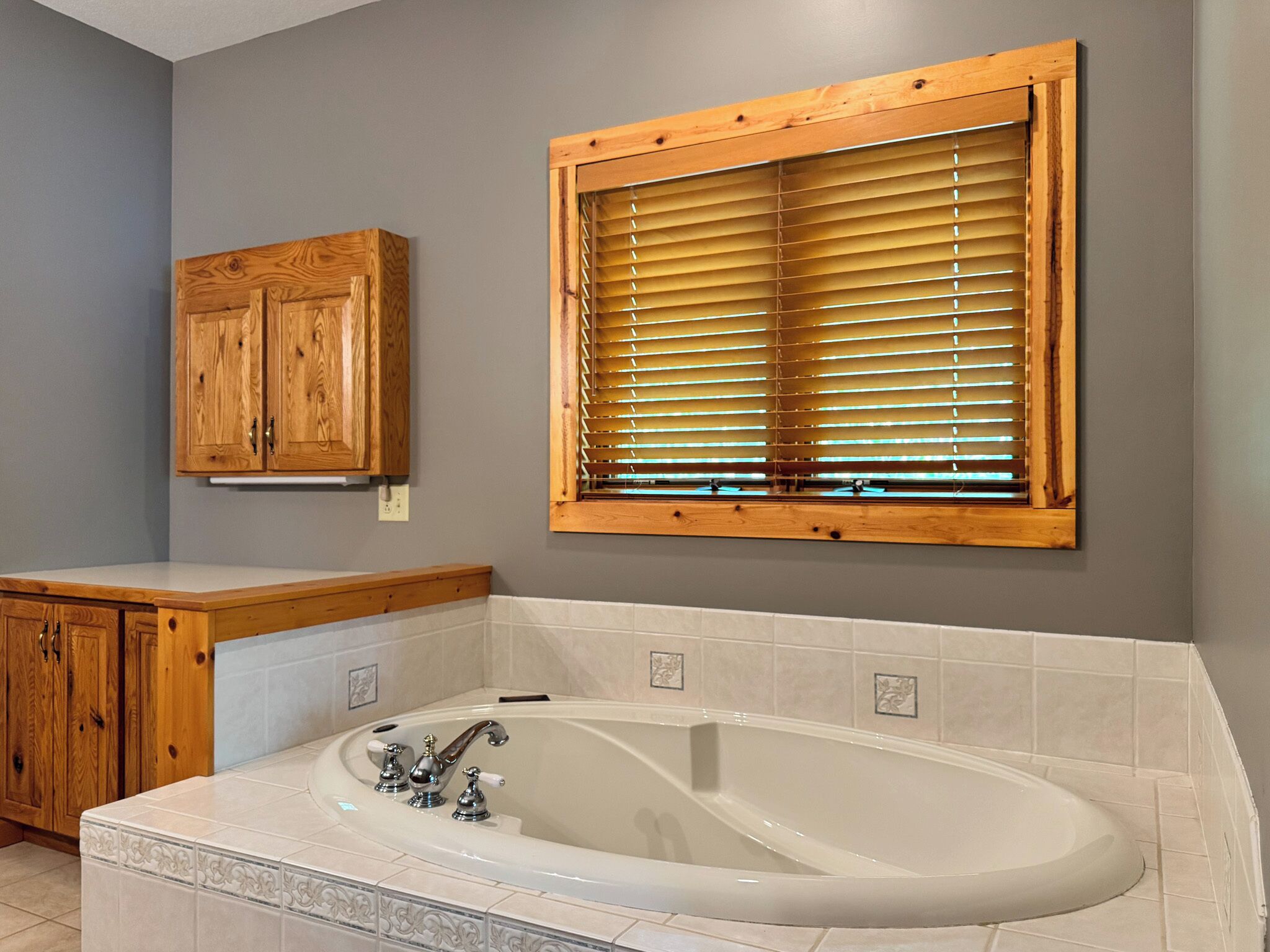 Un baño con bañera, armarios de madera y una ventana con persianas.