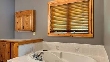 Un baño con bañera, armarios de madera y una ventana con persianas.