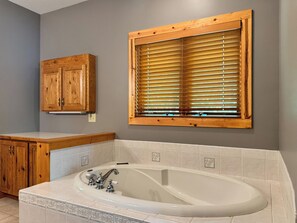 Un baño con bañera, armarios de madera y una ventana con persianas.