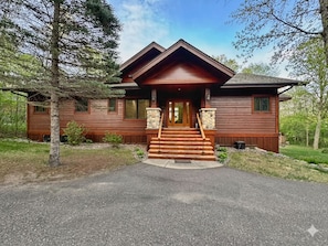 A wooden cabin with a front porch, stone accents, and a driveway leading to the entrance.