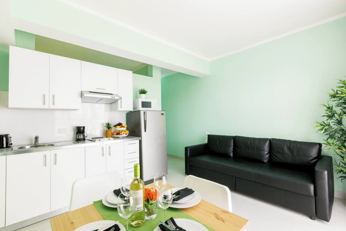A compact kitchen with white cabinets, a black leather sofa, and a dining table set for two.