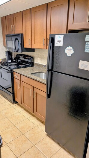 A kitchen with wooden cabinets, a black refrigerator, a stove, and a microwave. - Myrtle Beach ocean view condo, full kitchen, pools & hot tubs (Myrtle Beach)