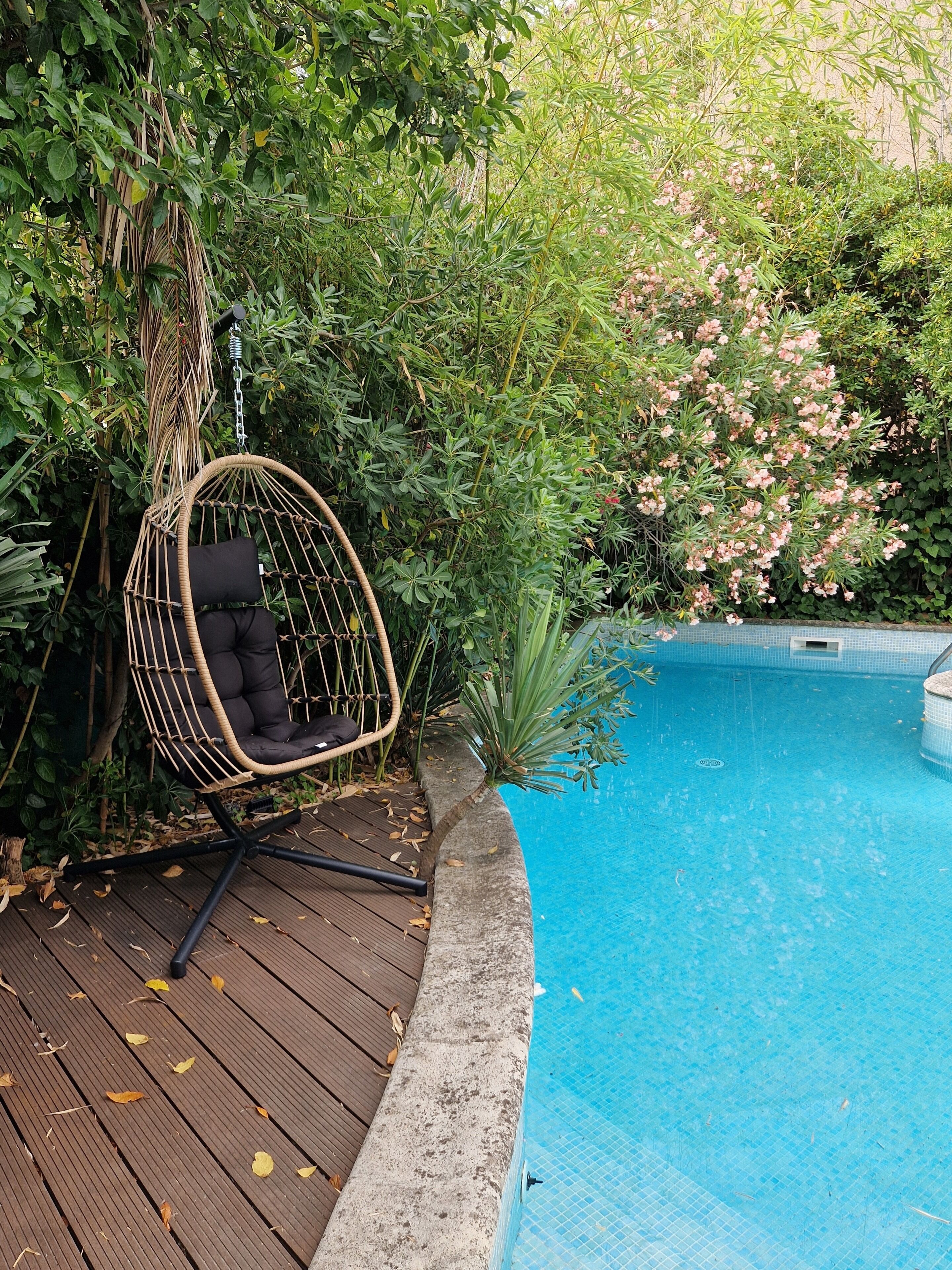 Una piscina con un pontile in legno e una sedia sospesa.