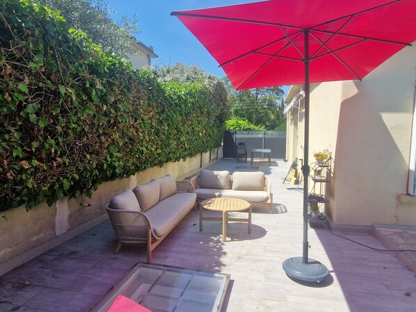 A patio with a sofa, a round table, and a red umbrella.
