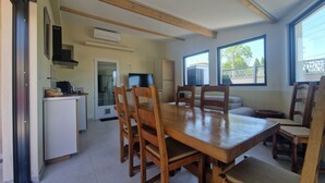 Un coin repas avec une table et des chaises en bois, un téléviseur et, au fond, une cuisine.