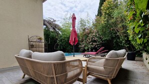 Une terrasse dotée de meubles en osier, d’une piscine et d’une végétation luxuriante.