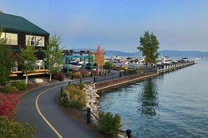 Une promenade en bord de mer, avec un bâtiment sur la gauche, un quai avec des bateaux, et une vue dégagée sur l’eau.