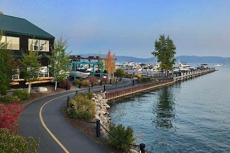 A waterfront walkway with a building on the left, a dock with boats, and a clear view of the water.