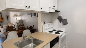 Ett kompakt kök med vita skåp, en spis, ett handfat och en matplats med ett träbord och stolar.