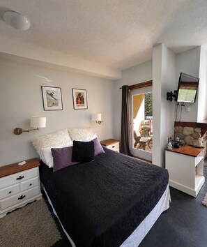 Une chambre à coucher comprenant un lit, deux lampes fixées au mur, un téléviseur et une porte donnant sur un espace extérieur.