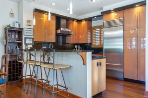 Eine moderne Küche mit Holzschränken, einem Edelstahlkühlschrank und einer Bar mit Hockern.