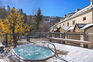 Ein Whirlpool in einer verschneiten Außenlandschaft mit Blick auf Gebäude und Bäume.