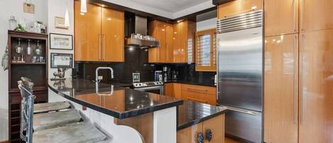 A modern kitchen with wooden cabinets, a stainless steel refrigerator, and a black countertop island.