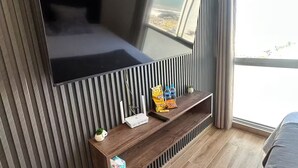 Ein modernes Schlafzimmer mit einem großen Wandfernseher, einem Holztischchen mit Snacks und einem großen Fenster mit Blick.
