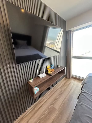 Ein modernes Schlafzimmer mit einem großen Wandfernseher, einem Holztischchen mit Snacks und einem großen Fenster mit Blick.