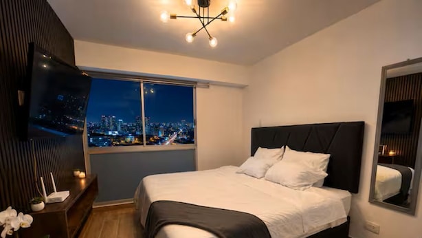 Ein Schlafzimmer mit Blick auf die Stadt, ein Bett, ein Fernseher und ein Nachttisch mit einer Pflanze.