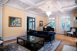A living room with a grand piano, a dark blue sofa, a coffee table, and a chandelier.