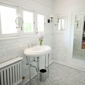 Un baño con un lavamanos blanco, dos espejos, un radiador y un cubo de basura.