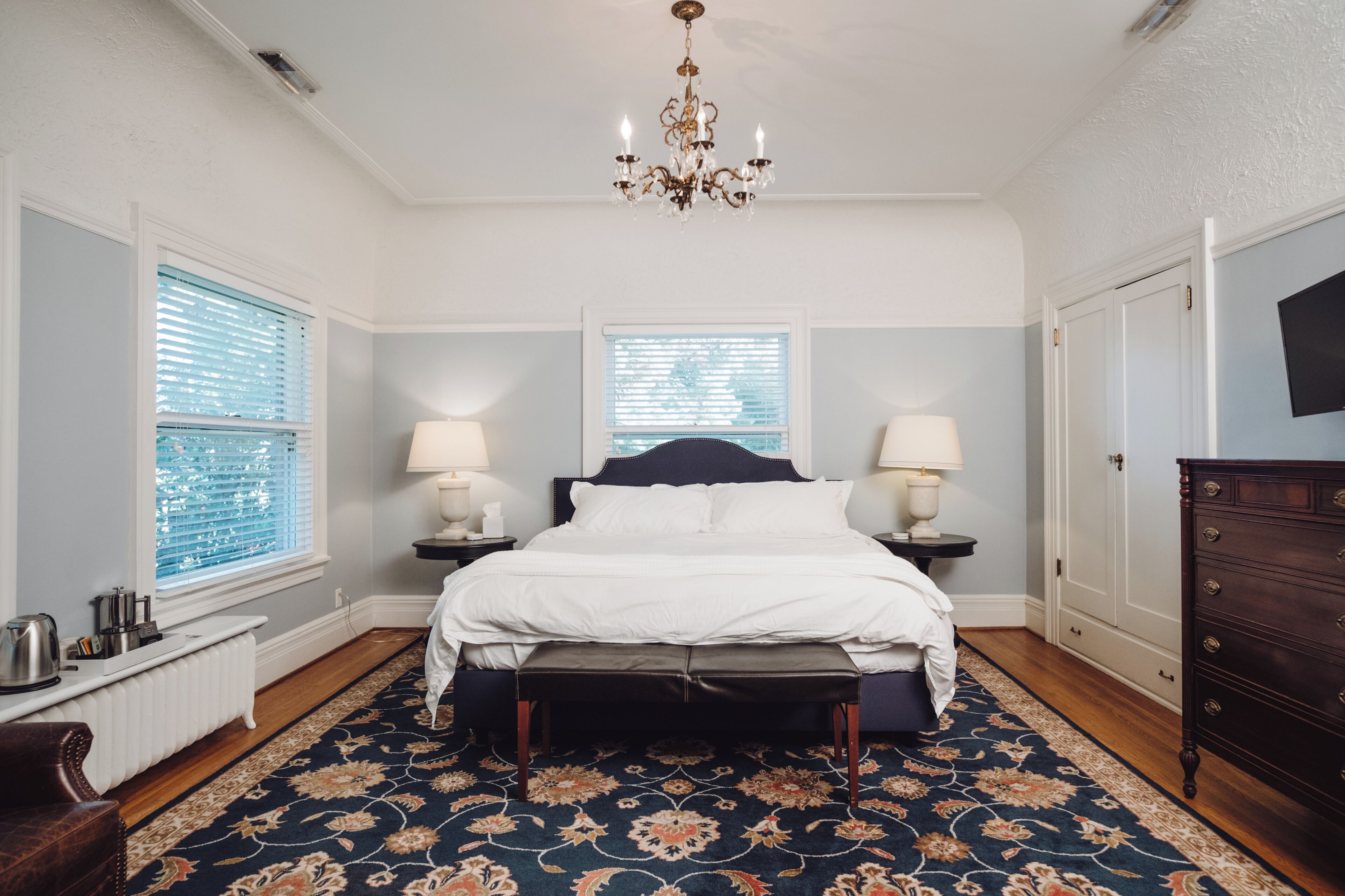 A bedroom with a large bed, two bedside tables with lamps, a chandelier, and a dresser.