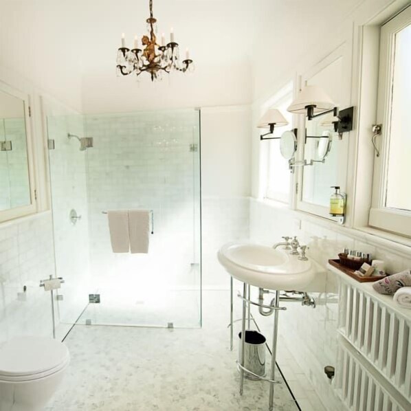 A modern bathroom with a glass shower enclosure, a white sink, and a chandelier.