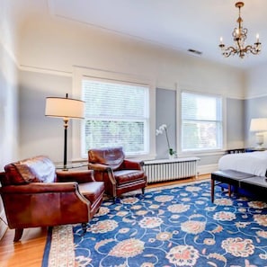 A room with a bed, two armchairs, a floor lamp, and a large window with blinds.