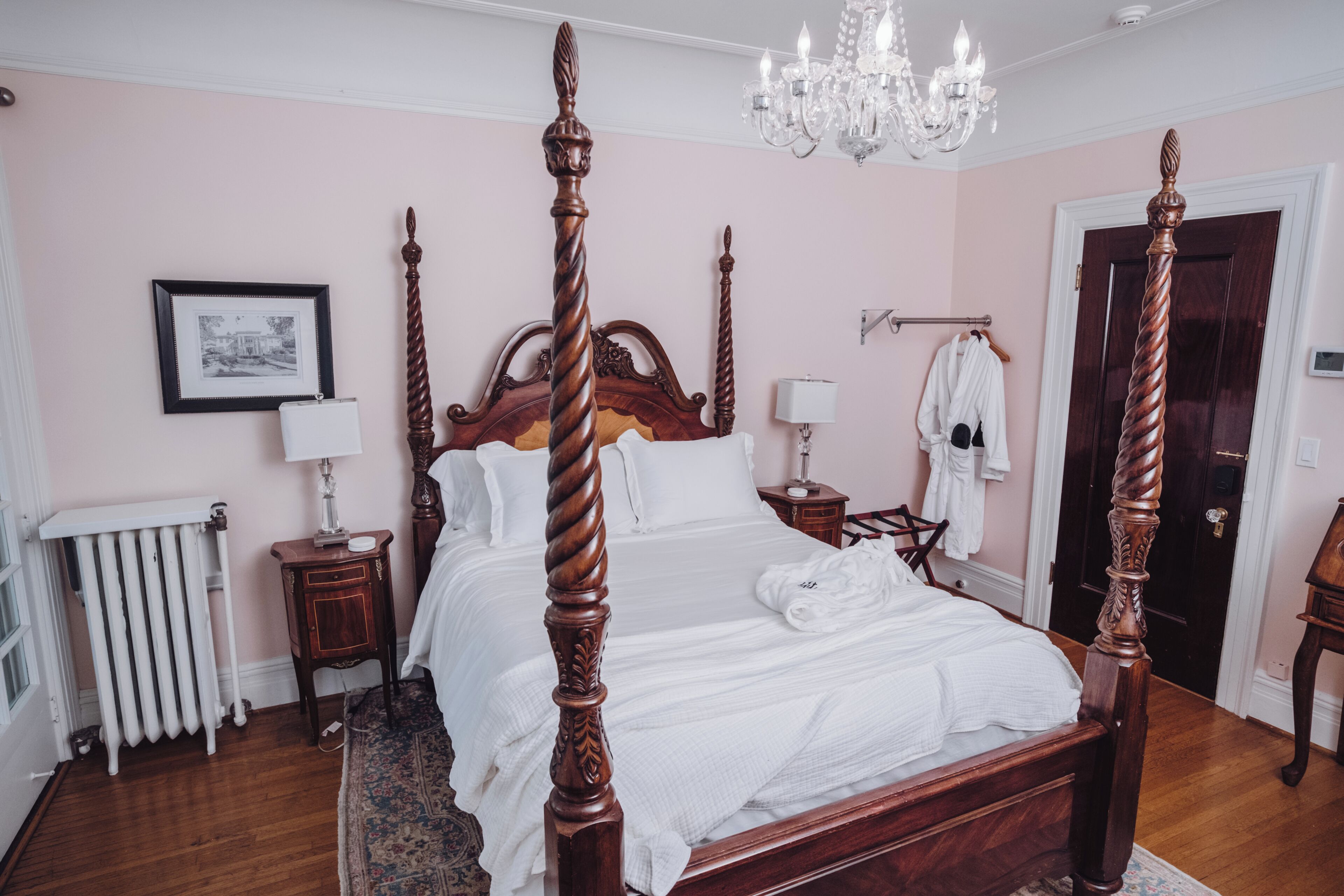 A four-poster bed with a chandelier, a radiator, and a framed picture on the wall.