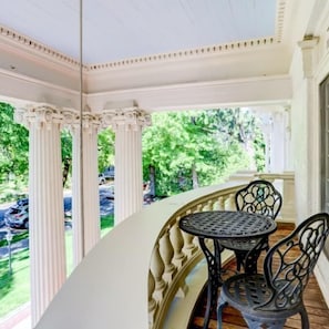 A covered porch with a round table and chairs, columns, and a view of greenery.
