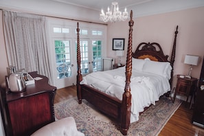 Ein Himmelbett mit Holz Kopfteil, eine Chandelier und Blick ins Freie durch eine Glastür.