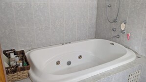 Et hvidt badekar med brusehoved, sæbeskål og håndbruser.