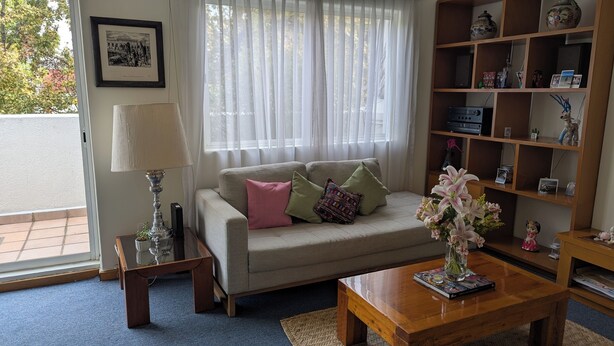En stue med sofa, sofabord, lampe, bogreol og et vindue med gardiner.
