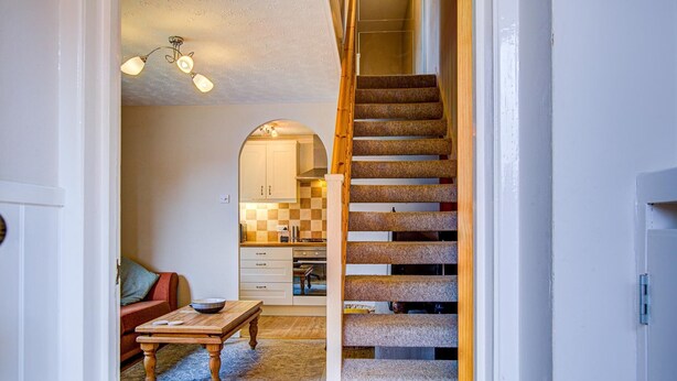 Eine Treppe führt zu einer Küche mit kariertem Fliesenspiegel, einem Holztisch mit Schüssel und einem Sofa in einem Flur.