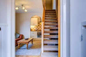A staircase leading to a kitchen with a checkered backsplash, a wooden table with a bowl, and a sofa in a hallway. - Cozy Home in Chelmsford - Pass the Keys (Chelmsford)