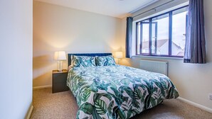 Ein Schlafzimmer mit einem Bett, zwei Nachttischlampen, einem Fenster mit Vorhängen und einer Heizung.