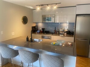 A modern kitchen with a central island, stainless steel appliances, and a clock on the wall. - Gorgeous 2-bedroom apartment in delightful Vancouver near FIFA & Canada Place (Vancouver)