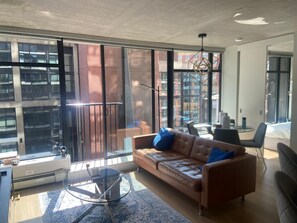 A modern living room with a leather sofa, a glass coffee table, and large windows offering views of a cityscape. - Gorgeous 2-bedroom apartment in delightful Vancouver near FIFA & Canada Place (Vancouver)