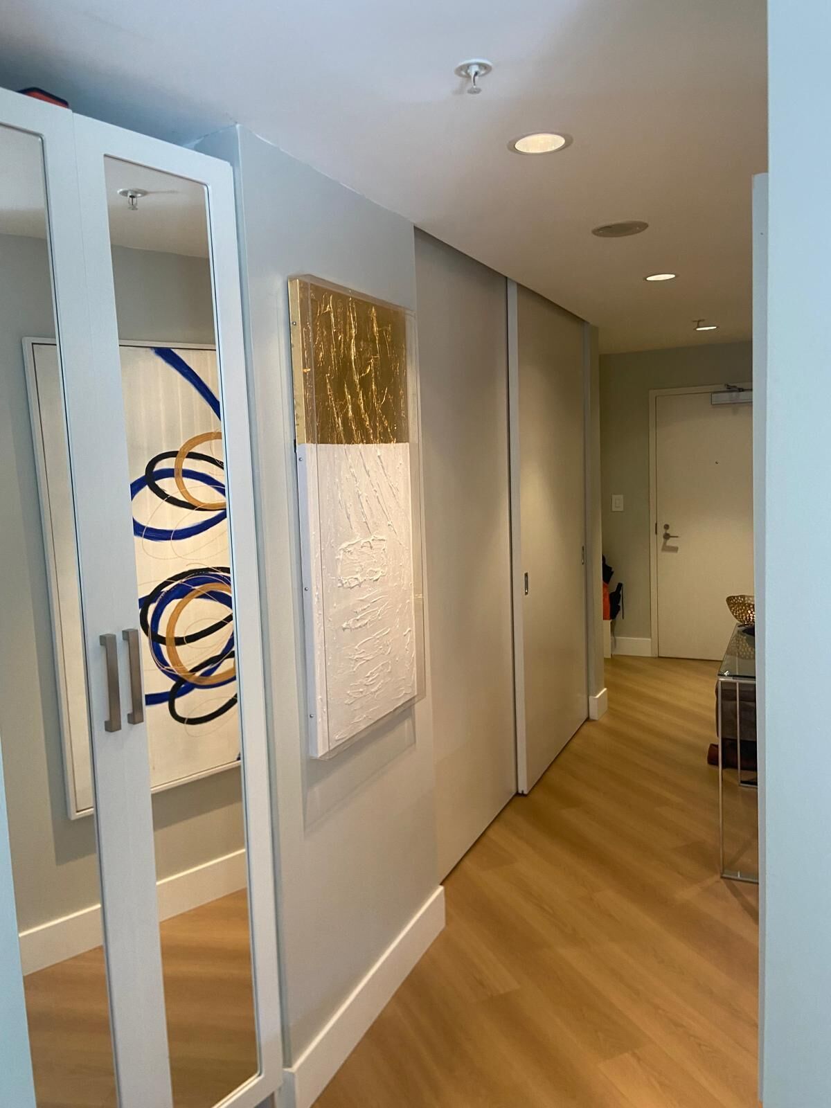 A hallway with a white door, a wall with abstract art, and a wooden floor.