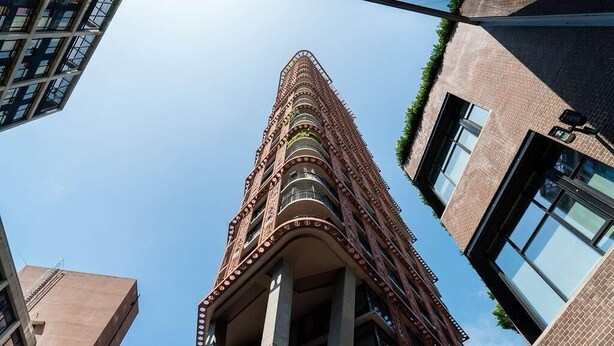 Un edificio alto de varios pisos con un diseño arquitectónico único, con balcones y un cielo despejado al fondo.