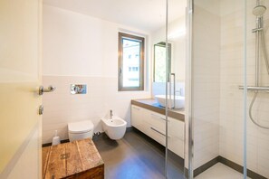 Une salle de bain moderne équipée de toilettes, d’un bidet, d’un meuble-lavabo et d’une douche séparée par une paroi en verre.