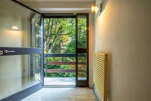 Un couloir moderne avec une porte en verre donnant sur un balcon d’où l’on peut admirer la vue sur les arbres.