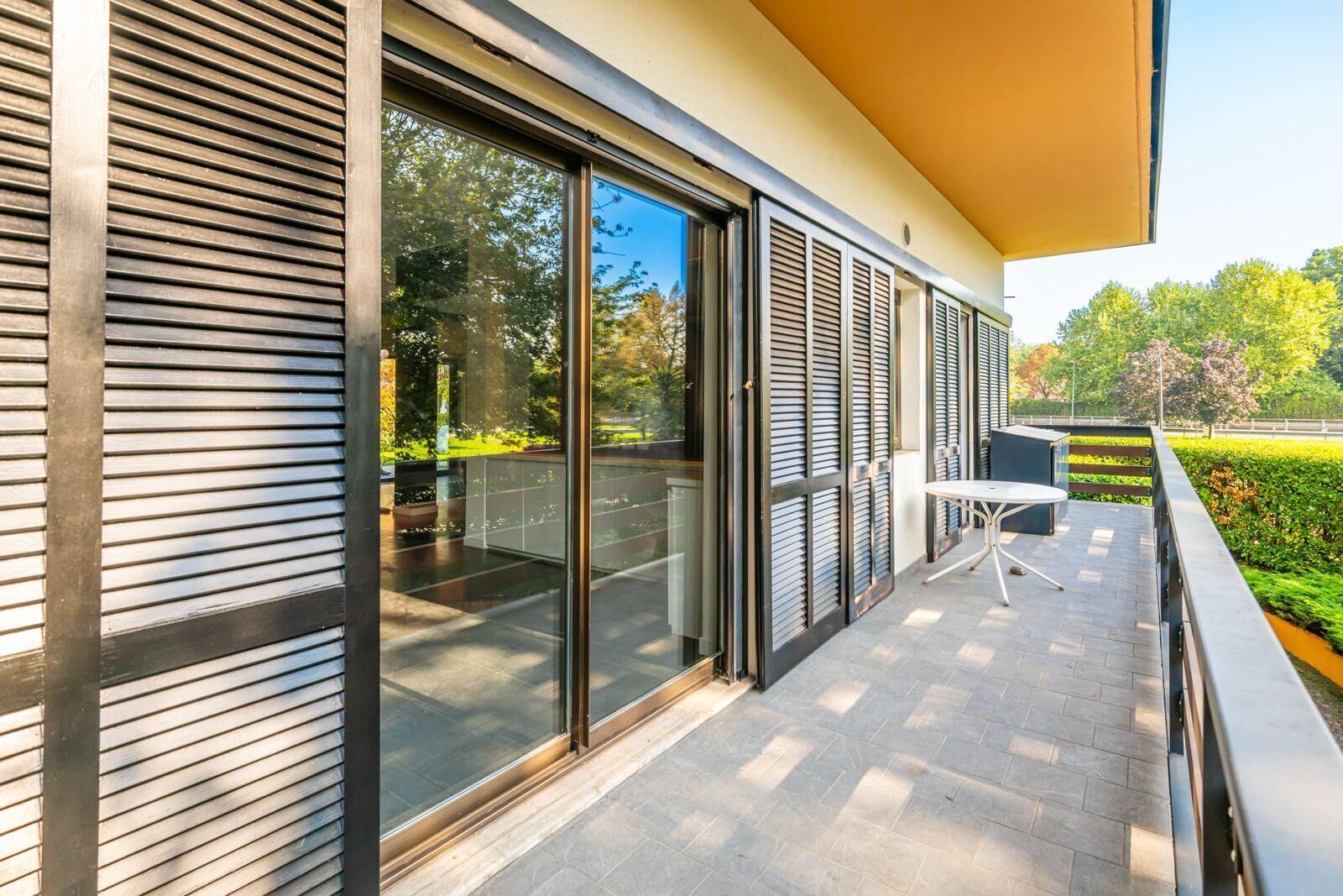 Un edificio moderno con ampie porte scorrevoli in vetro, una piccola zona con posti a sedere all'aperto e un giardino curato.
