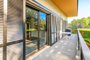 Un edificio moderno con ampie porte scorrevoli in vetro, una piccola zona con posti a sedere all'aperto e un giardino curato.